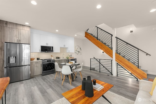 kitchen featuring white cabinets, sink, light hardwood / wood-style flooring, decorative backsplash, and appliances with stainless steel finishes