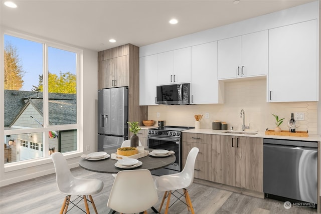 kitchen featuring white cabinets, sink, light wood-type flooring, appliances with stainless steel finishes, and tasteful backsplash