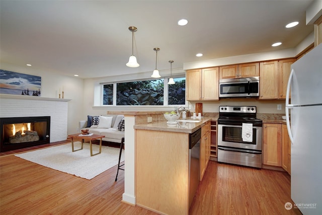 kitchen with light brown cabinets, light hardwood / wood-style floors, decorative light fixtures, a kitchen bar, and appliances with stainless steel finishes