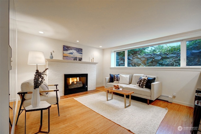 living room with wood-type flooring, a baseboard radiator, and a brick fireplace