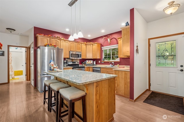 kitchen with appliances with stainless steel finishes, a center island, light hardwood / wood-style flooring, and hanging light fixtures