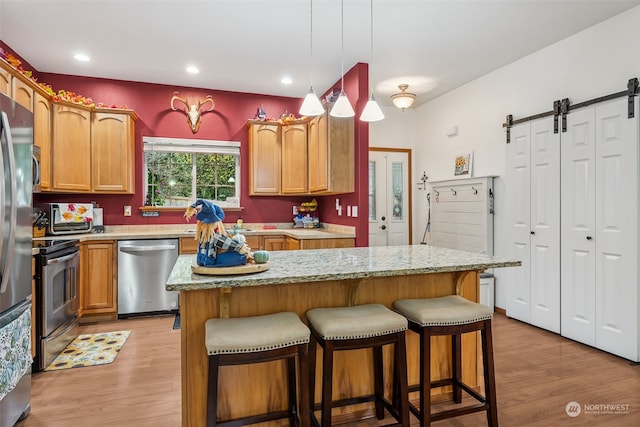 kitchen with a barn door, a kitchen island, stainless steel appliances, and light wood-type flooring