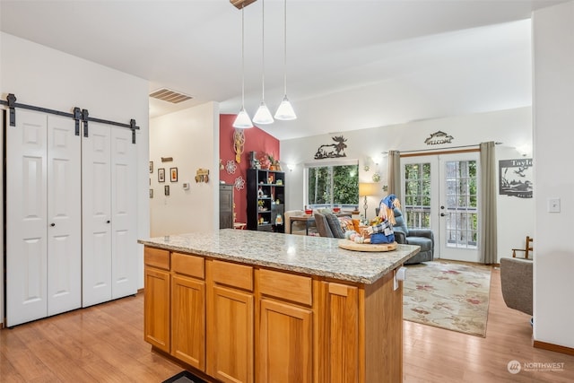 kitchen with light stone countertops, a barn door, light hardwood / wood-style flooring, a kitchen island, and hanging light fixtures