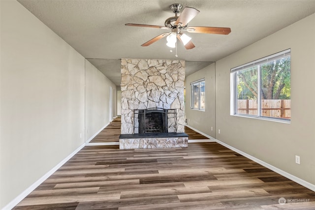 unfurnished living room with hardwood / wood-style floors, a textured ceiling, a stone fireplace, and ceiling fan