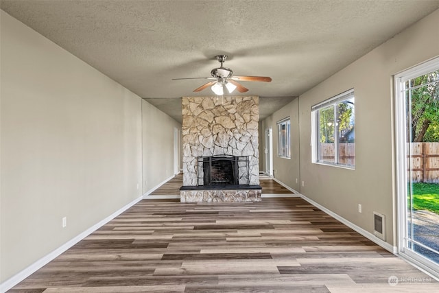 unfurnished living room with a textured ceiling, light wood-type flooring, a stone fireplace, and ceiling fan