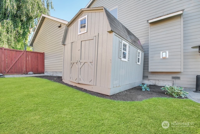 view of side of home with a shingled roof, a gambrel roof, fence, a storage unit, and a yard