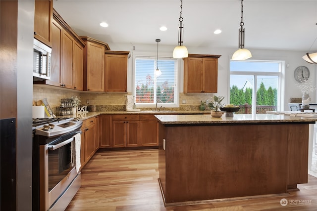 kitchen with appliances with stainless steel finishes, brown cabinets, light stone counters, and decorative light fixtures