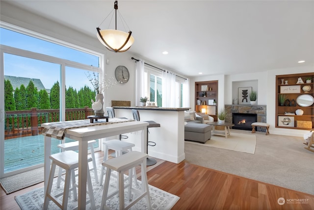 dining space featuring light wood-style floors, recessed lighting, built in shelves, and a stone fireplace