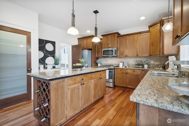 kitchen with appliances with stainless steel finishes, a kitchen island, a sink, and pendant lighting