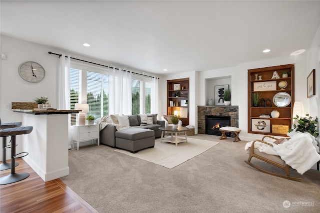 living room with a stone fireplace, built in features, and light hardwood / wood-style flooring