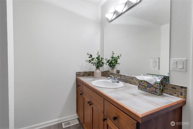 bathroom featuring baseboards, visible vents, backsplash, and vanity