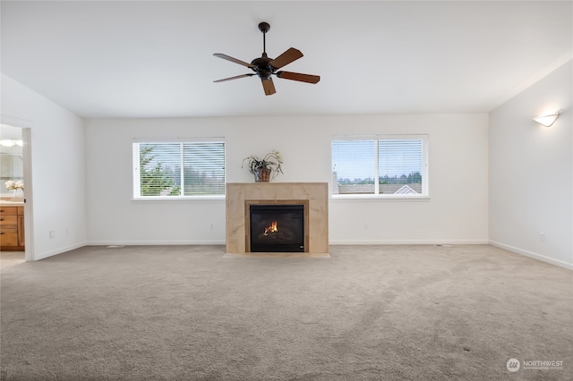 unfurnished living room featuring ceiling fan, light colored carpet, a wealth of natural light, and a tiled fireplace