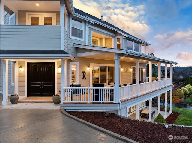 back house at dusk featuring covered porch