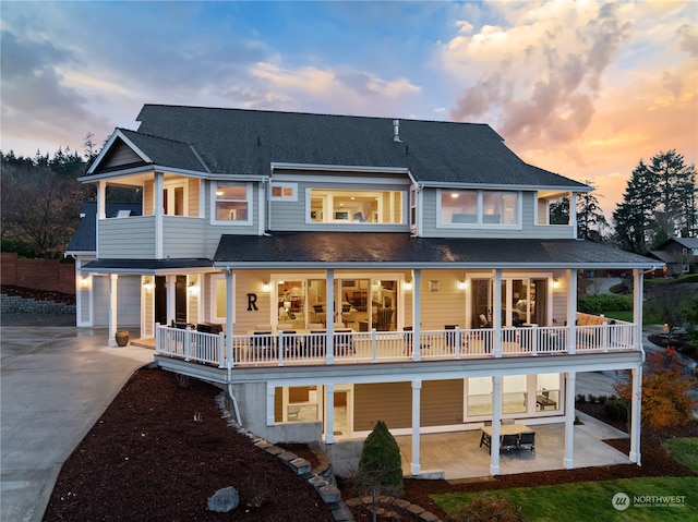 back of property at dusk featuring a patio area, a shingled roof, driveway, and a balcony