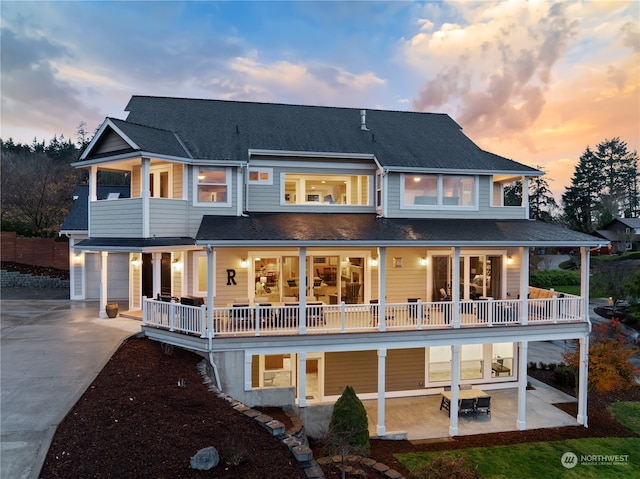 back house at dusk featuring a balcony, a patio, and a garage