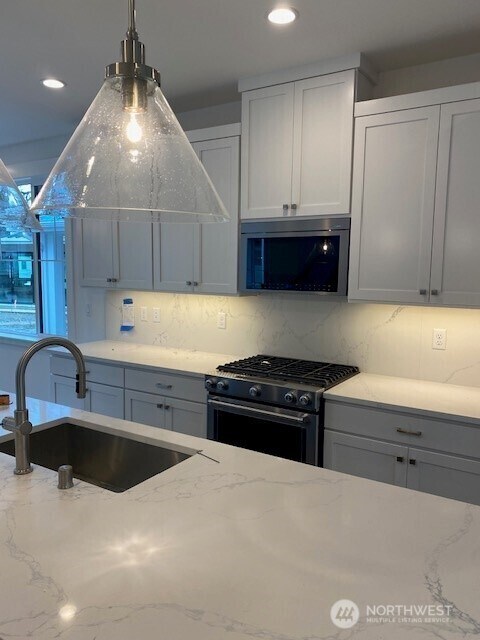 kitchen featuring appliances with stainless steel finishes, a sink, backsplash, and light stone counters