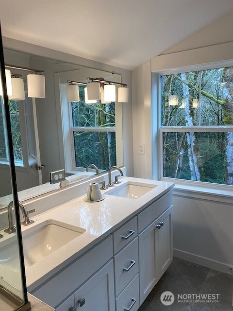 bathroom featuring lofted ceiling, a sink, baseboards, and double vanity