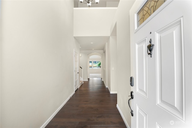 corridor with a towering ceiling, a chandelier, and dark hardwood / wood-style floors