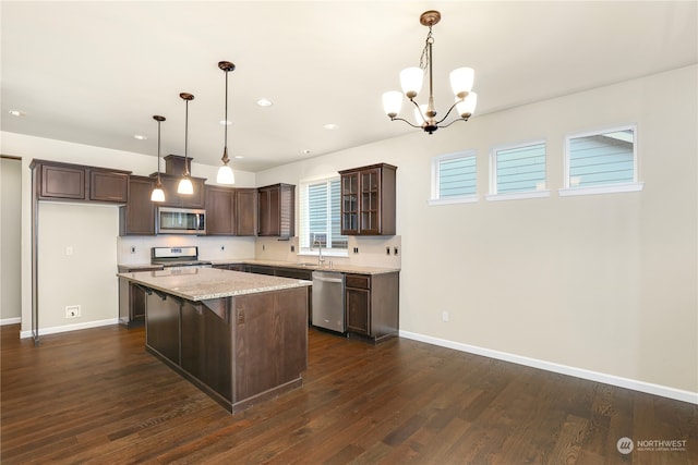 kitchen with dark wood-type flooring, hanging light fixtures, light stone countertops, a kitchen island, and stainless steel appliances