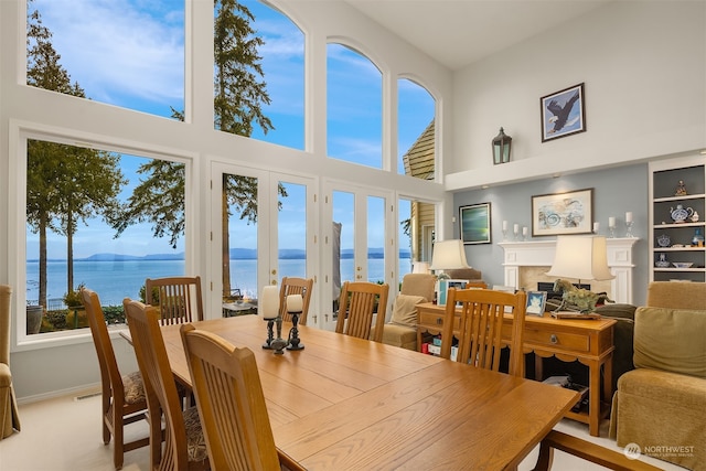 dining space featuring carpet floors, french doors, a water view, and a high ceiling