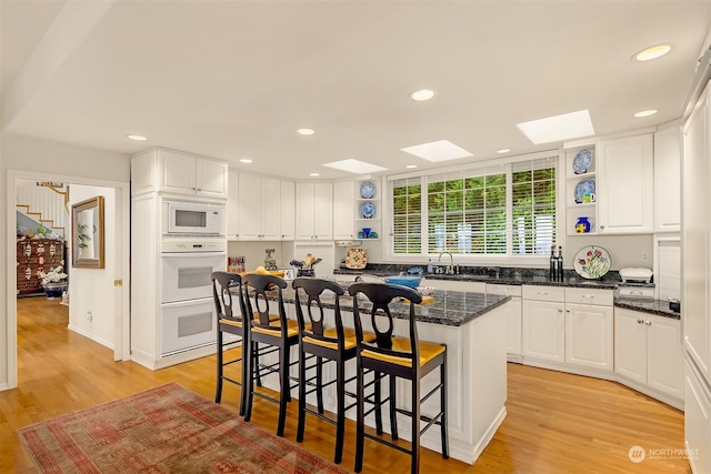 kitchen featuring a skylight, white cabinetry, a kitchen island, and light hardwood / wood-style floors