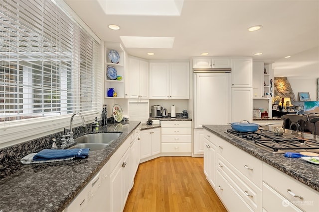 kitchen featuring a skylight, sink, light hardwood / wood-style floors, stainless steel gas stovetop, and white cabinets