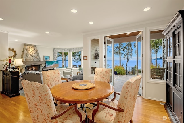 dining room with a fireplace, ornamental molding, light wood-type flooring, and a healthy amount of sunlight