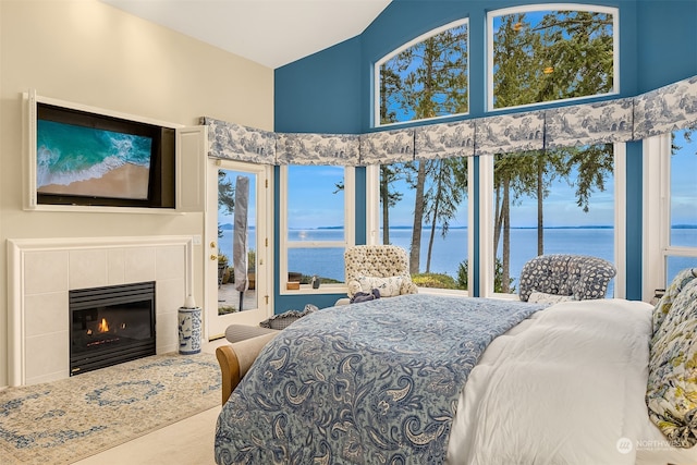 carpeted bedroom with a towering ceiling, a water view, multiple windows, and a tiled fireplace