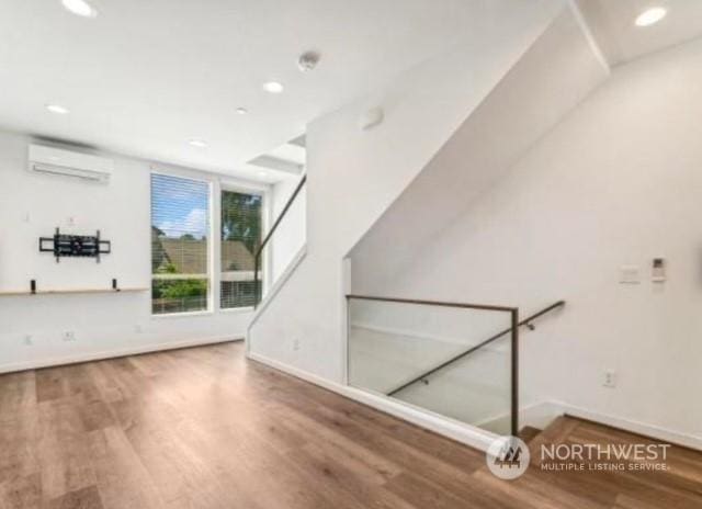 additional living space featuring a wall mounted air conditioner and hardwood / wood-style floors