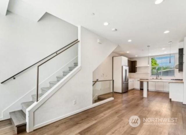 kitchen with white cabinets, hardwood / wood-style floors, stainless steel refrigerator, and pendant lighting