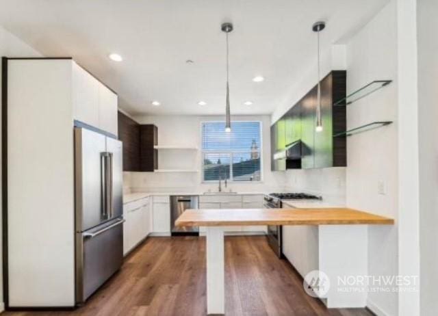 kitchen featuring wood-type flooring, appliances with stainless steel finishes, decorative light fixtures, white cabinetry, and butcher block counters