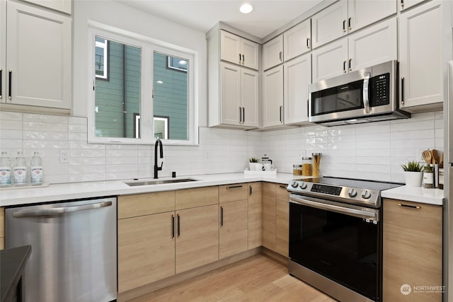 kitchen featuring appliances with stainless steel finishes, light wood-type flooring, tasteful backsplash, sink, and light brown cabinets