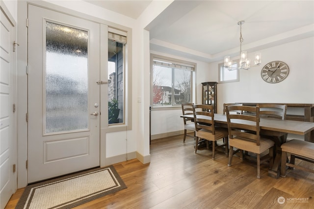 dining space with wood-type flooring, a raised ceiling, and a notable chandelier