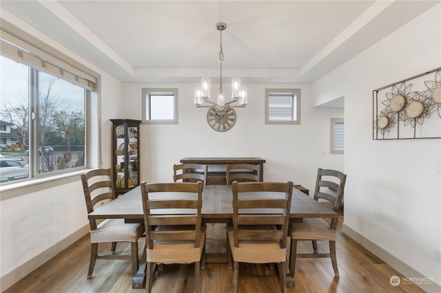 dining space with hardwood / wood-style floors, a raised ceiling, and a notable chandelier