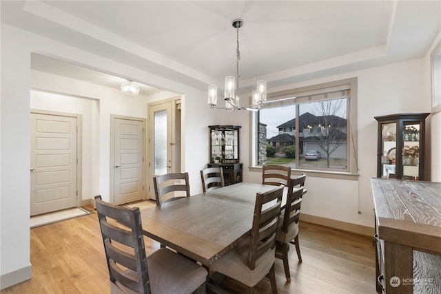 dining area featuring light wood-type flooring, a tray ceiling, and a chandelier