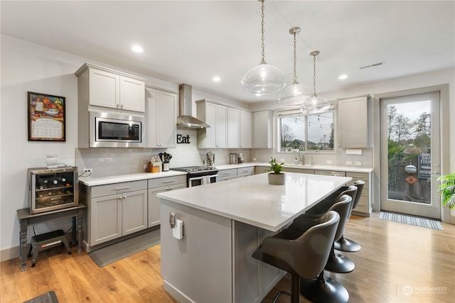 kitchen featuring a center island, wall chimney exhaust hood, hanging light fixtures, appliances with stainless steel finishes, and light wood-type flooring