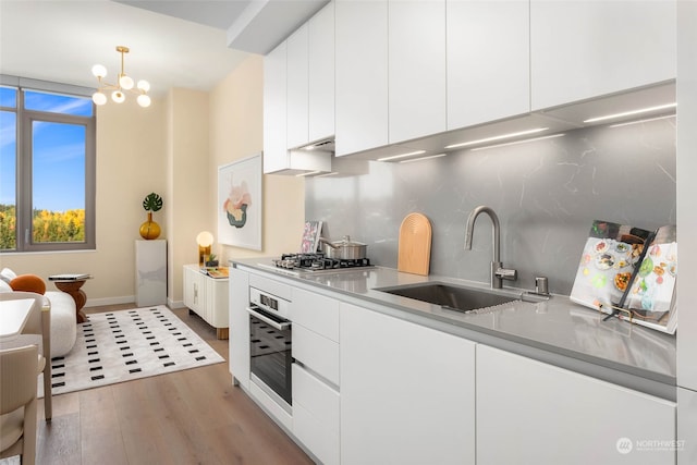 kitchen featuring decorative light fixtures, sink, white cabinets, light hardwood / wood-style floors, and stainless steel appliances