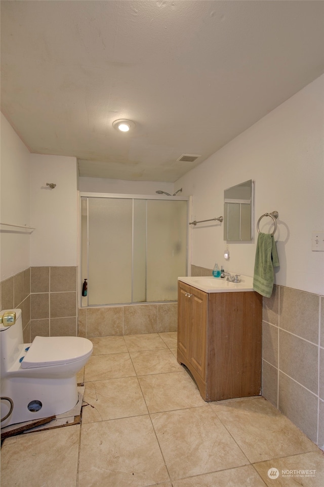 bathroom featuring vanity, a shower with door, tile walls, tile patterned flooring, and toilet