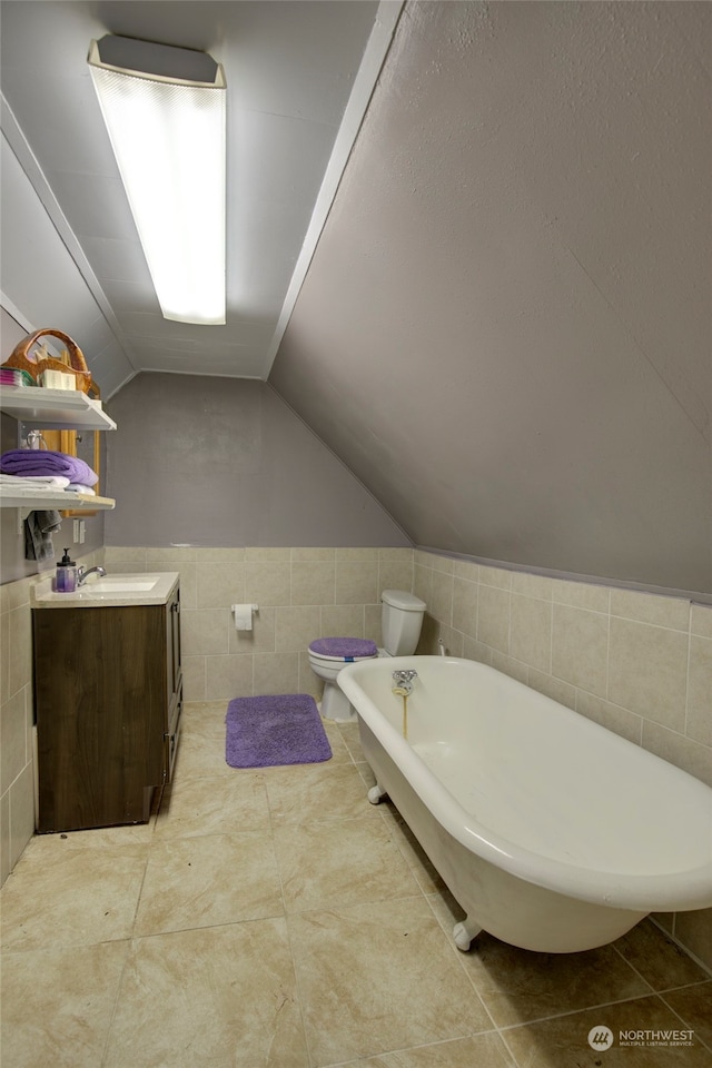 bathroom featuring tile patterned floors, vanity, tile walls, toilet, and lofted ceiling