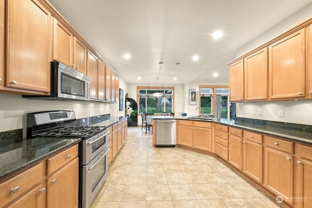 kitchen featuring kitchen peninsula, stainless steel appliances, dark stone countertops, and sink