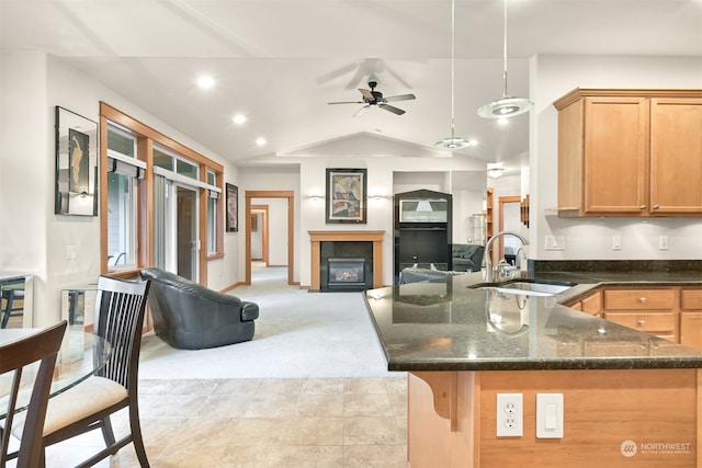 kitchen featuring dark stone counters, light colored carpet, vaulted ceiling, sink, and pendant lighting