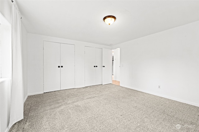 unfurnished bedroom featuring light carpet and two closets