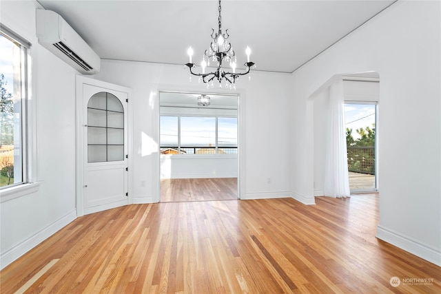 unfurnished dining area featuring light wood-type flooring, a wall unit AC, a healthy amount of sunlight, and a notable chandelier