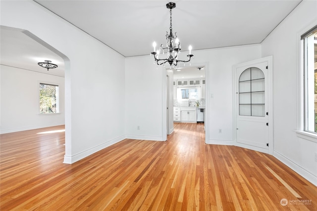 unfurnished dining area with sink, ornamental molding, light hardwood / wood-style floors, and a notable chandelier