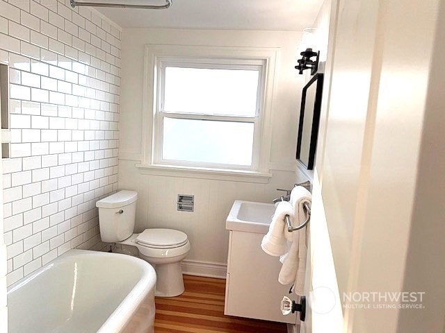 bathroom featuring vanity, a bathing tub, toilet, tile walls, and wood-type flooring