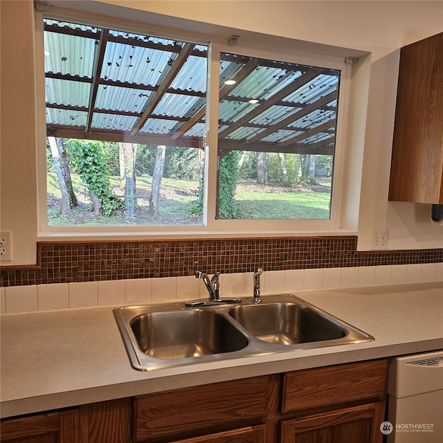 kitchen featuring backsplash, dishwashing machine, and sink