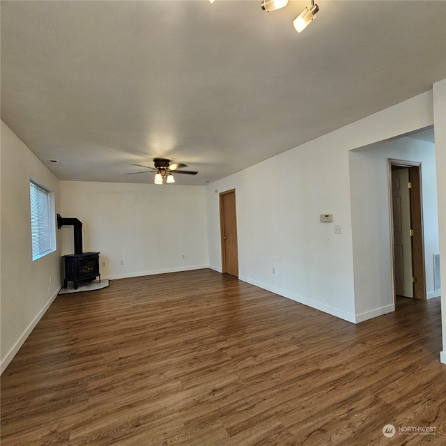 unfurnished living room with dark hardwood / wood-style flooring, a wood stove, and ceiling fan