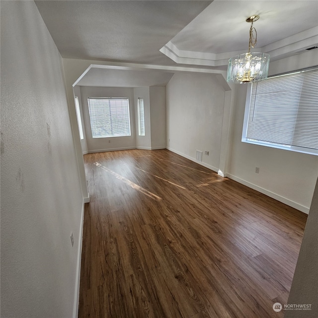 interior space with a raised ceiling, dark hardwood / wood-style flooring, and an inviting chandelier