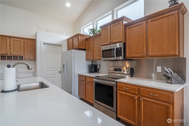 kitchen featuring light stone countertops, sink, stainless steel appliances, tasteful backsplash, and vaulted ceiling