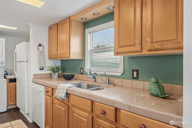 kitchen featuring dark hardwood / wood-style flooring, white appliances, stacked washing maching and dryer, and tile counters